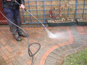 A man using a pressure washer to clean an exterior brick patio.
