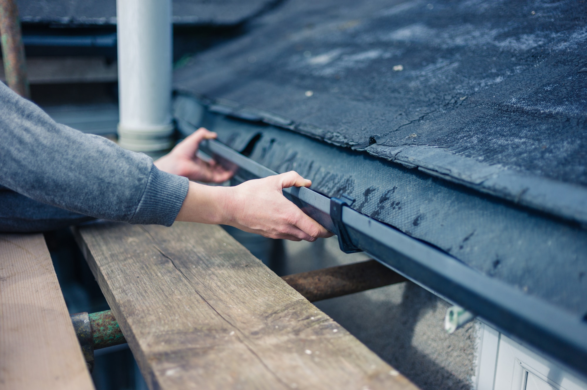 Gutter cleaning, reasons, A man performing exterior cleaning and fixing a gutter on a roof.
