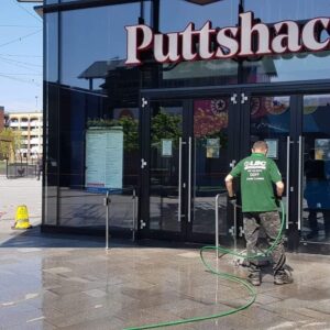 Pressure Washing Services A man performing commercial cleaning on the exterior of a putschka store.