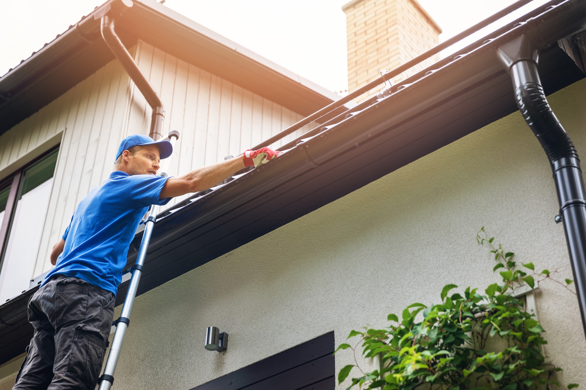roof cleaning, myths, A man performing exterior cleaning of a house, including gutter and roof cleaning.