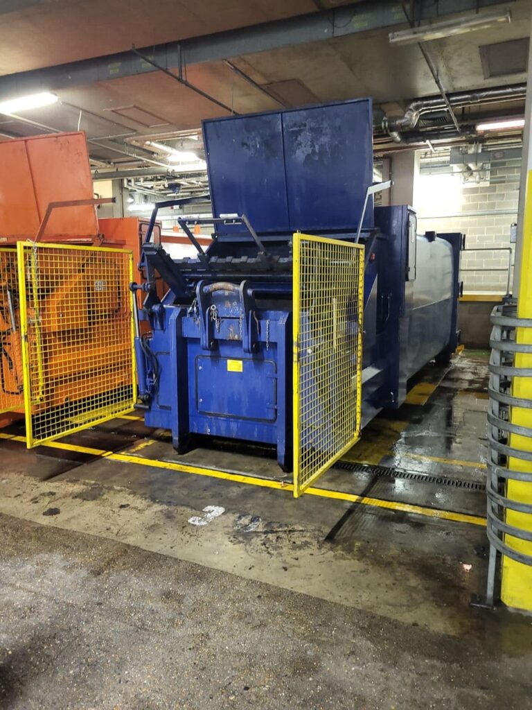 Compactor Cleaning, A blue and orange machine in a garage used for exterior cleaning.